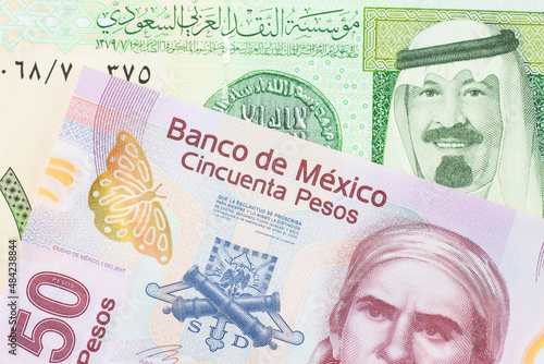 A macro image of a pink, plastic fifty peso bank note from Mexico paired up with a green and yellow on riyal bank note from Saudi Arabia. Shot close up in macro.