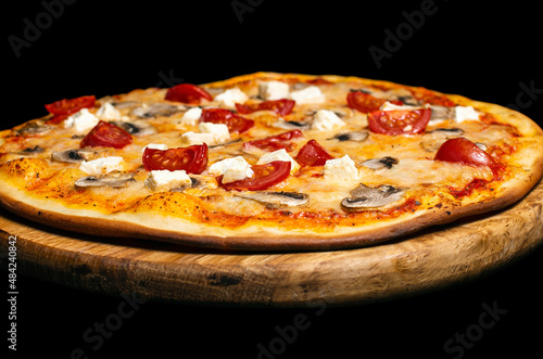 Pizza with a variety of ingredients: cheese, tomatoes, mushrooms, feta cheese. On a wooden board