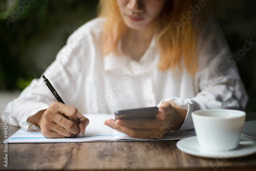 Work from home concept. Planner using phone and noted plan daily agenda on calendar book. Woman Hand mark and write schedule (holiday trip) on diary at business office desk. Coffee place on table