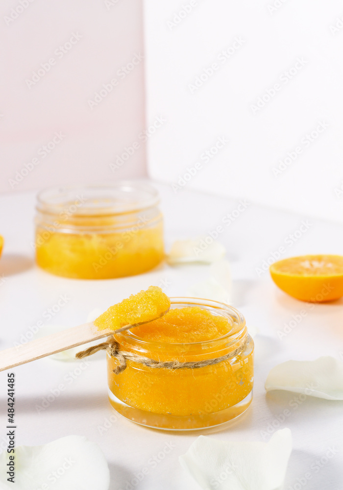 Homemade cosmetic scrub for peeling and cleansing the skin of the body in a glass package on a white background with orange citrus fruits and flower petals. Homemade cosmetic scrub for peeling and cleansing the skin of the body in a glass package on a white background with orange citrus fruits and flower petals.