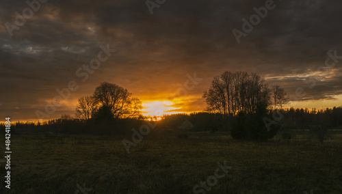 Glorious sunset through clouds over field and trees silhouettes