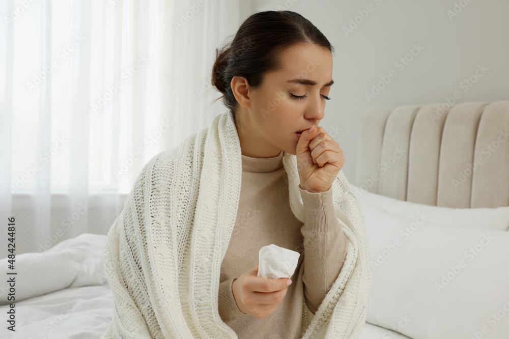 Sick young woman with tissue wrapped in knitted plaid at home Sick young woman with tissue wrapped in knitted plaid at home