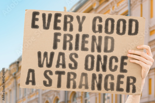 The phrase " Every good friend was once a stranger " on a banner in men's hand with blurred sea on the background. Associate. Union. Walk. Community. Access. Connecting. Communication. Brotherhood