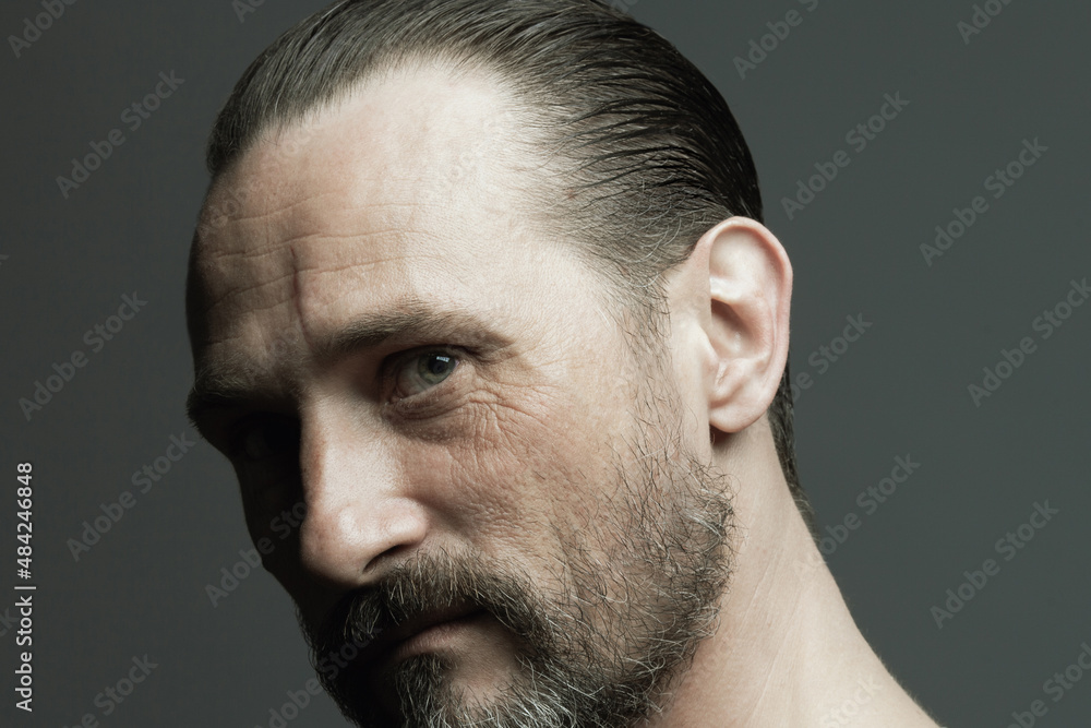Male beauty concept. Fabulous at any age. Portrait of 45-year-old man standing over dark gray background. Hair brushed back. Rocker, biker style. Scar on forehead. Close up. Studio headshot Male beauty concept. Fabulous at any age. Portrait of 45-year-old man standing over dark gray background. Hair brushed back. Rocker, biker style. Scar on forehead. Close up. Studio headshot