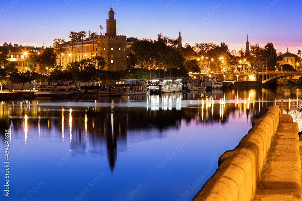 Golden sunrise seen from the Guadalquivir river boulevard in Triana in downtown Seville with a view on the golden tower and perfect reflections in the water.
