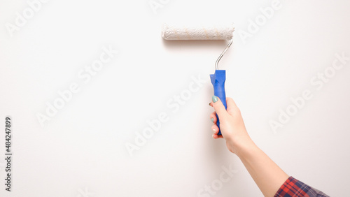 Painting works. A woman paints a light wall with a paint roller. Close-up on a hand with a tool. Construction worker, tool, apartment renovation.