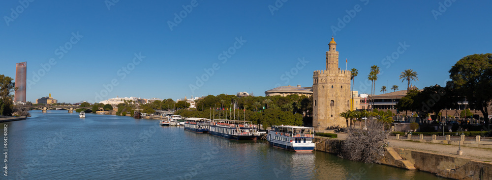 Obraz premium The golden tower in the Centre of Seville alongside the river. The golden tower as it was named, is a popular spot to start a walk on the boulevard