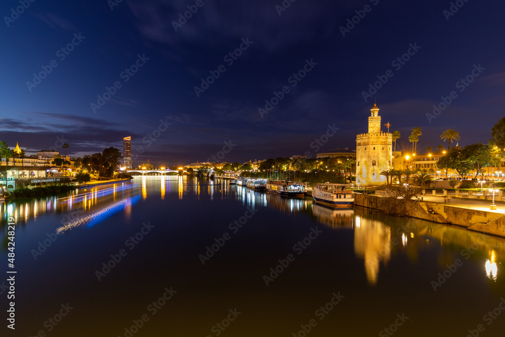 Sunset over the river Guadalquivir in downtown Seville with amazing colors in the sky and a view on the riverside of the Triana neighbourhood and the illuminated golder tower