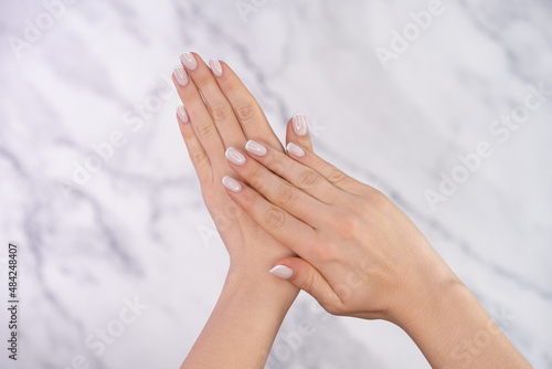 Beautiful female hands with french manicure on nails. Soft skin, skincare, beauty treatment concept. Young woman applying cream or lotion onto graceful hands with slender fingers on light background