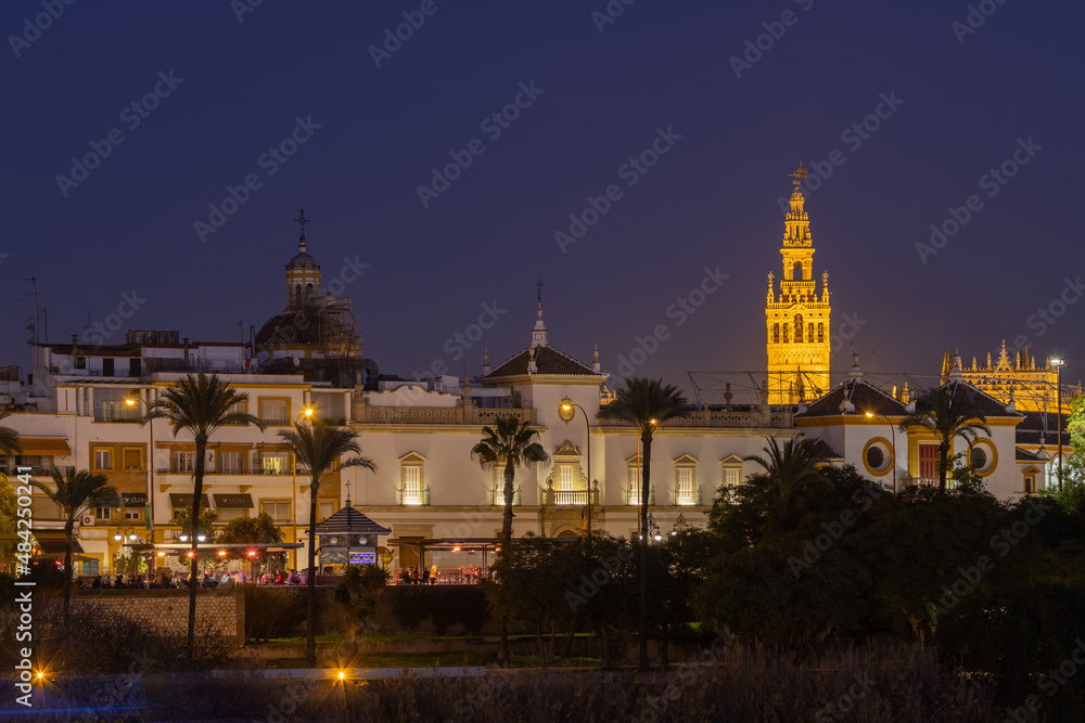 The illuminated Giralda (english Giralda) tower in downtown Seville during the blue hour seen for the river bank of the  Guadalquivir river.