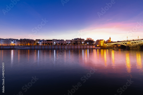 Sunset over the river Guadalquivir in downtown Seville with amazing colors in the sky and a view on the riverside of  the Triana neighbourhood.