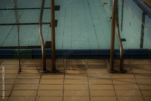 Schwimmbad Panorama mit Rundgeländer aus Metall auf beigen Beckenuferbodenkacheln vor blauem Schwimmbecken mit schwarzen Streifen im Herbst  photo