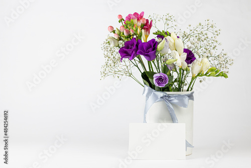 Beautiful Spring, summer flowers in vintage ceramic vase with ribbon, and Blank greeting card on white background.  Mock up, empty copy space.