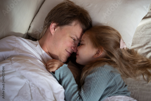 little cute girl hugging her dad while lying in bed