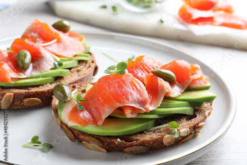 Delicious sandwiches with salmon, avocado and capers on plate, closeup