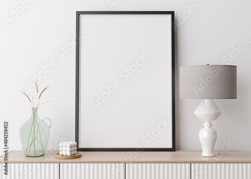 Empty vertical picture frame on white wall in modern living room. Mock up interior in contemporary style. Free space for picture, poster. Console, lamp, glass vase with grass, candle. 3D rendering. © Creative_Bird