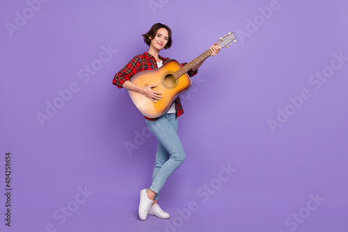 Full length photo of cute young brunette lady stand with guitar wear shirt jeans footwear isolated on purple background