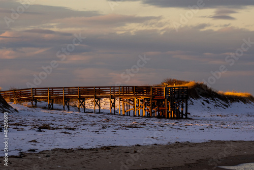 Sunlit pier on snowy beach © Lesli Woodruff