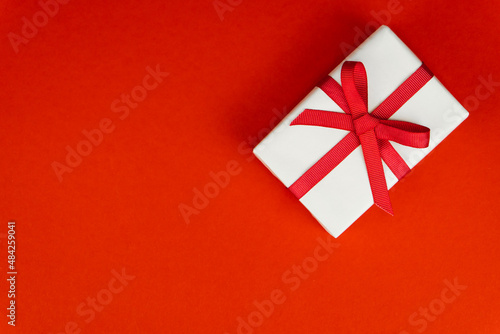 Valentine's Day or birthday concept with copy space. White gift box with red ribbon on red papper