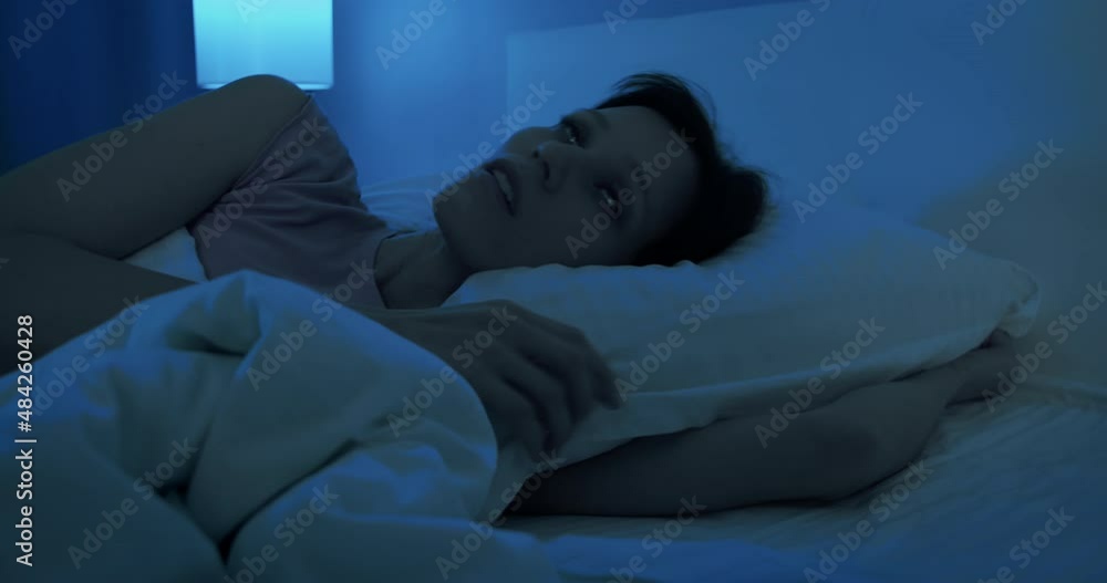 Brunette woman in pajamas lying in bed sleepless late at night, insomnia Brunette woman in pajamas lying in bed sleepless late at night, insomnia