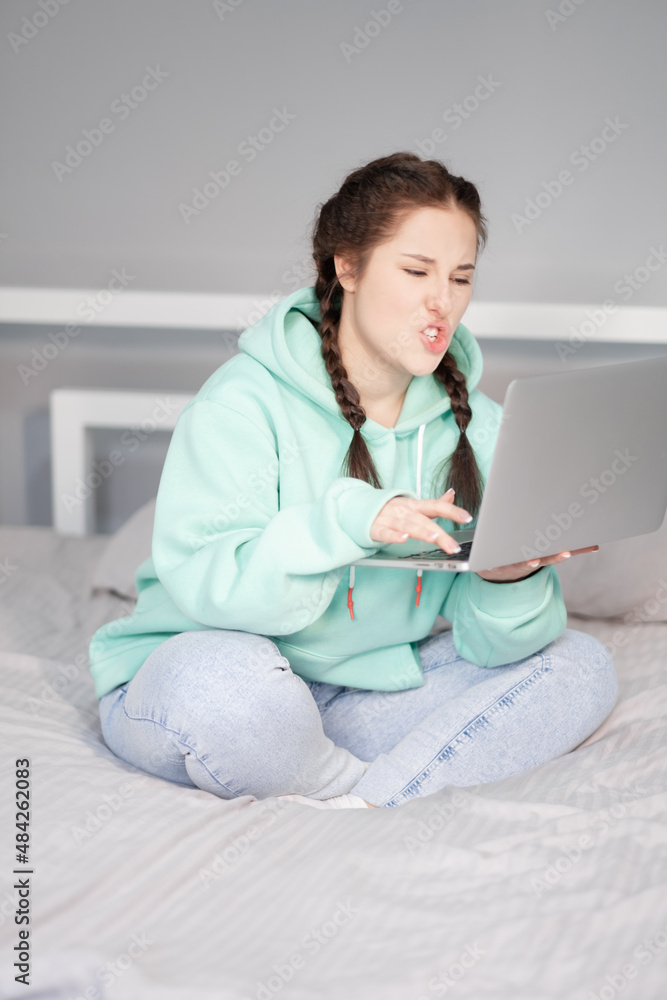 Distance learning online education and work. Happy woman girl in turquoise hoodie and jeans working office work remotely from home on white bed. Using computer laptop Distance learning online education and work. Happy woman girl in turquoise hoodie and jeans working office work remotely from home on white bed. Using computer laptop