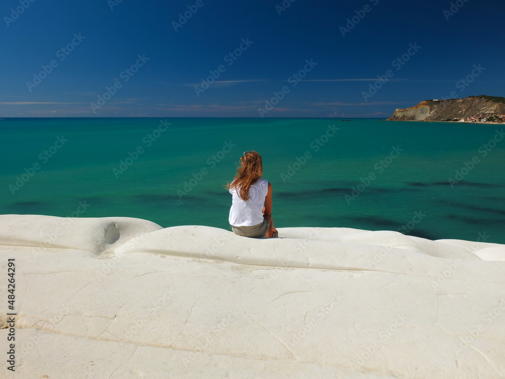 Young woman sitting at the top of Scala dei Turchi in Sicily with a nice view of green sea