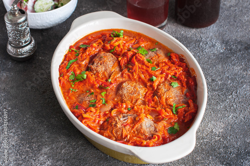 Homemade meat cutlets with tomato sauce in a baking dish on a gray background.