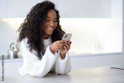 African American smiling Girl using smartphone on modern kitchen at home, pressing finger, reading social media internet, typing text or shopping online, Mobile phone in two black hands
