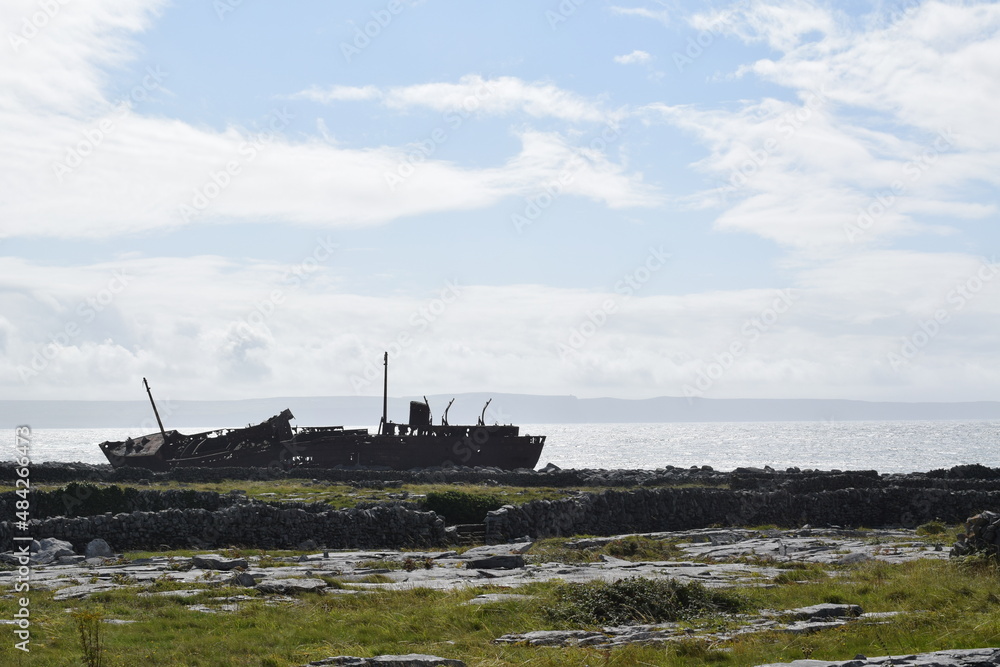 Plassey Shipwreck. Ship stranded on rocks. Ship silhouette on a sunny summer day. Bright panorama with sky and clouds on the background. Inisheer Island. Ireland. Plassey Shipwreck. Ship stranded on rocks. Ship silhouette on a sunny summer day. Bright panorama with sky and clouds on the background. Inisheer Island. Ireland.