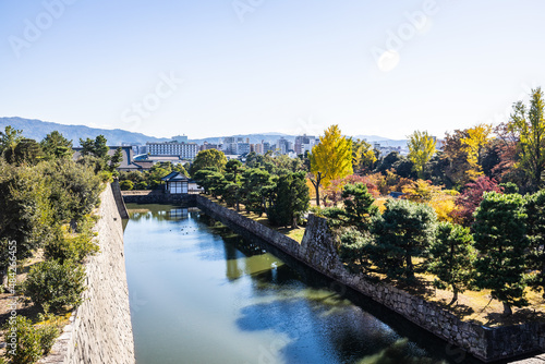The moat of Nijo Castle with the city of Kyoto in the background and fall colors on the trees in daylight.