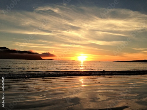 Impressive summer sunset on a beach. Sea and light reflection on water. Ramberg, Lofoten, Norway.