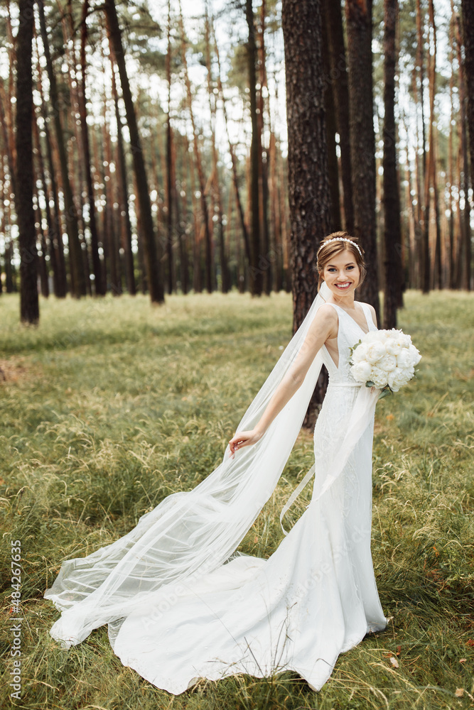 an elegant bride stands in the forest and holds a beautiful wedding bouquet with a peony in her hands an elegant bride stands in the forest and holds a beautiful wedding bouquet with a peony in her hands