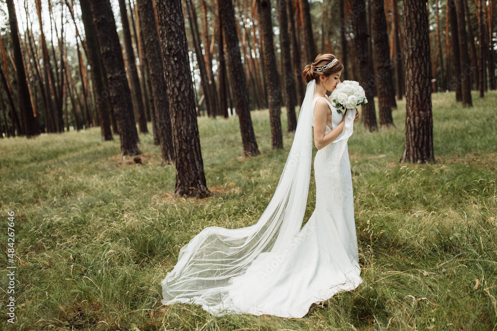 an elegant bride stands in the forest and holds a beautiful wedding bouquet with a peony in her hands