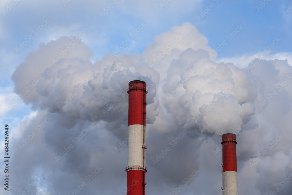 two red-white chimneys with the release of a large amount of smoke and steam against the blue sky two red-white chimneys with the release of a large amount of smoke and steam against the blue sky