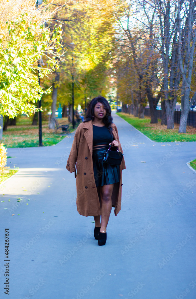 Fototapeta premium Front view of a beautiful African lady wearing a black dress in a park.