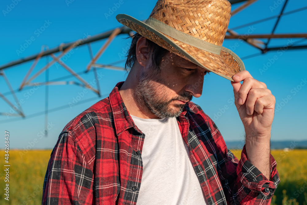 Fototapeta premium Portrait of serious farmer standing in front of center-pivot irrigation equipment in rapeseed field