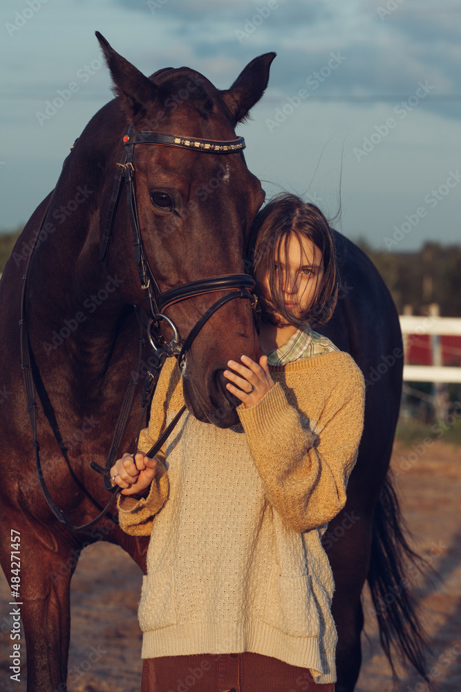 Obraz premium A young girl with a short haircut next to her horse at sunset. Good friends. Summer and happiness.