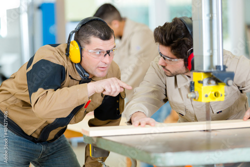 experienced carpenter guiding apprentice using bench saw