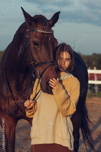 A young girl with a short haircut next to her horse at sunset. Good friends. Summer and happiness.