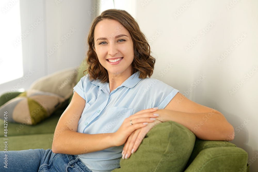 Close-up portrait on brunette-haired woman in home interior. Charming young caucasian lady looking at camera and smiles, resting, serene female spending weekend at home Close-up portrait on brunette-haired woman in home interior. Charming young caucasian lady looking at camera and smiles, resting, serene female spending weekend at home
