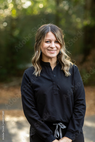 A young cosmetologist standing outside among green trees for a headshot with copy space