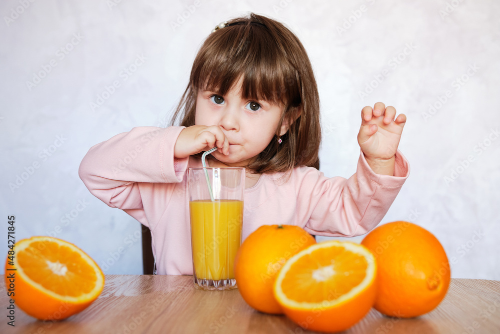 Cute baby girl drinking glass of fresh orange juice indoors. Cute baby girl drinking glass of fresh orange juice indoors.