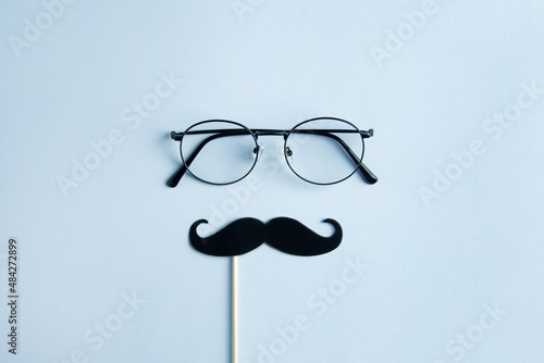 Father's Day Holiday Concept. Transparent glasses, stylish black paper photo booth props moustaches on blue background. 