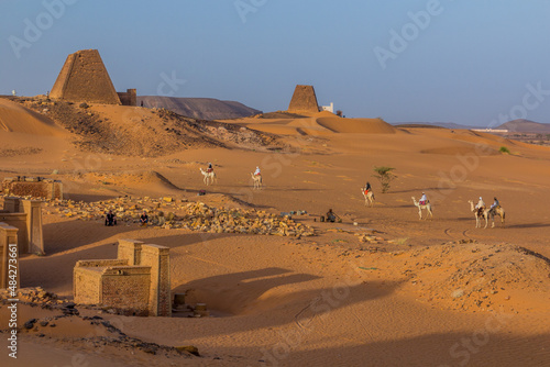 MEROE, SUDAN - MARCH 4, 2019: Locals on camels near Meroe pyramids, Sudan photo