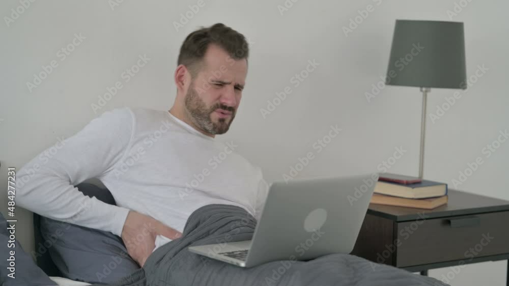 Man with Back Pain working on Laptop in Bed Man with Back Pain working on Laptop in Bed