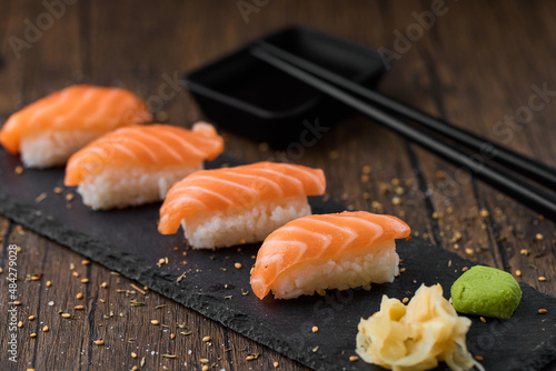 Set of salmon sushi, fried shrimps and rolls served on a black stone plate on a wooden table with chopsticks and soy sauce. 