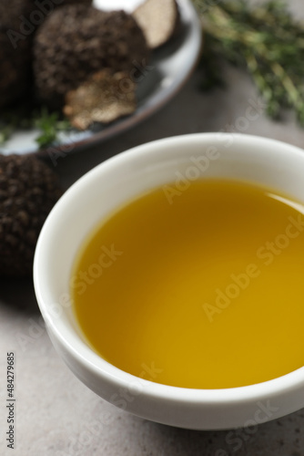 Fresh truffle oil in bowl on light grey table, closeup