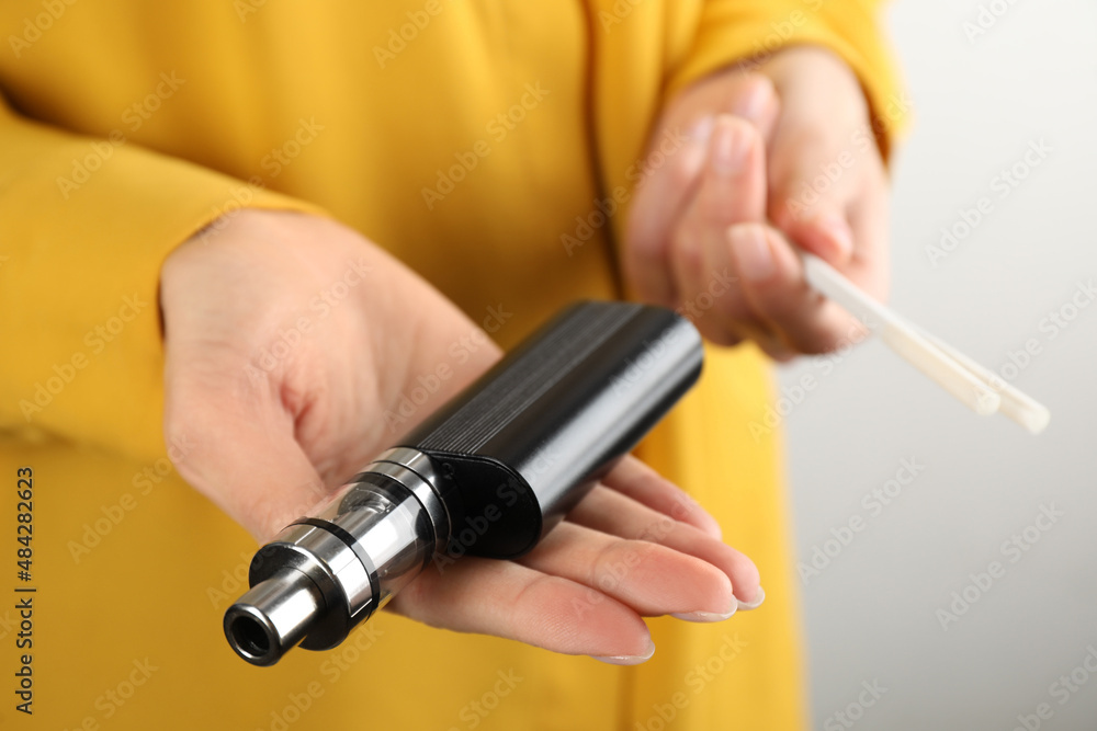 Woman with cigarettes and vaping device on light background, closeup. Smoking alternative Woman with cigarettes and vaping device on light background, closeup. Smoking alternative