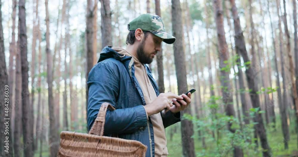 Young man mushroom picker walking in unknown forest looking for mushrooms stands in middle of trees with basket and phone, trying to get range, no signal, compass, navigation, lost, can't find way out Young man mushroom picker walking in unknown forest looking for mushrooms stands in middle of trees with basket and phone, trying to get range, no signal, compass, navigation, lost, can't find way out