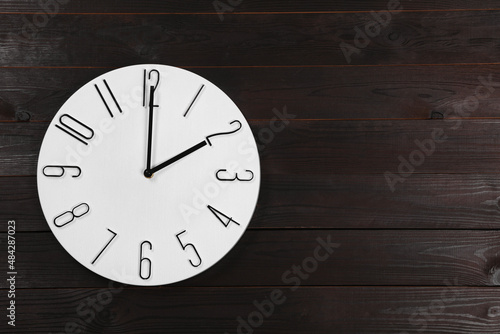 Stylish analog clock hanging on wooden wall, space for text